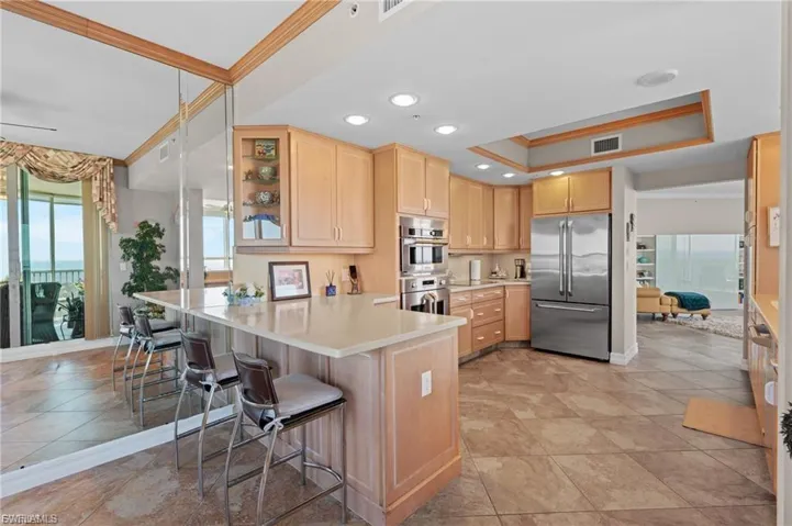 Kitchen with healthy amount of natural light, light brown cabinets, light countertops, crown molding, and appliances with stainless steel finishes