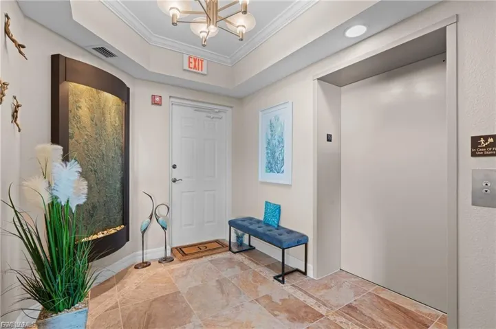 Private foyer entrance featuring elevator, ornamental molding, a raised ceiling, and a chandelier