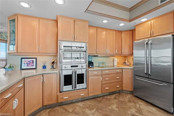 Kitchen with appliances with stainless steel finishes, recessed lighting, light brown cabinets, glass insert cabinets, and ornamental molding