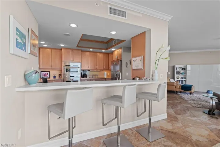 Kitchen with a kitchen breakfast bar, ornamental molding, appliances with stainless steel finishes, a tray ceiling, and light countertops