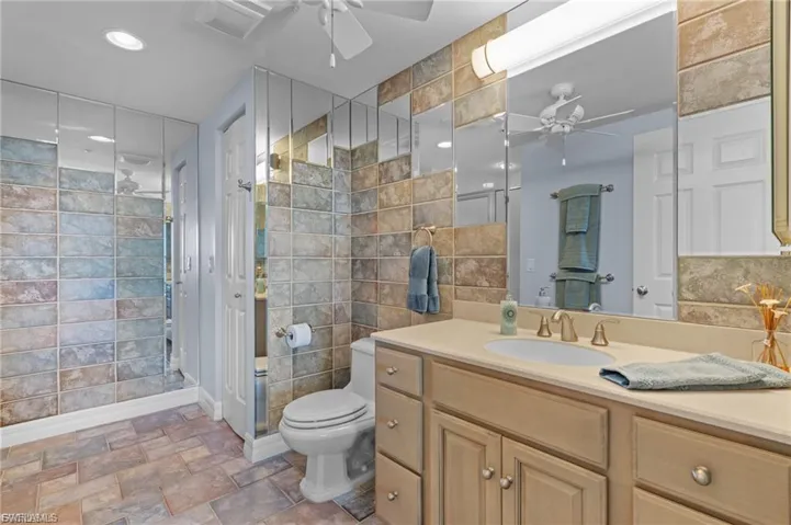 Full bath with ceiling fan, vanity, tile walls, stone finish floors, and a stall shower