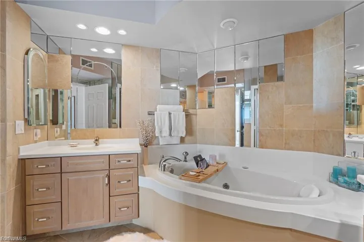 Bathroom with tile walls, a tub with jets, vanity, a stall shower, and recessed lighting