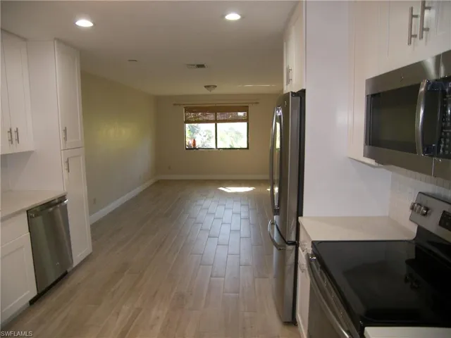 Kitchen with backsplash, white cabinetry, light hardwood / wood-style floors, and appliances with stainless steel finishes