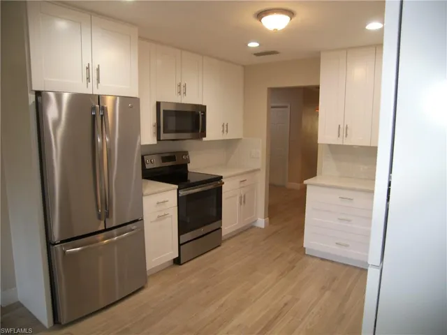 Kitchen featuring backsplash, stainless steel appliances, white cabinetry, and light hardwood / wood-style floors