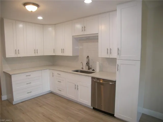 Kitchen with white cabinets, light hardwood / wood-style floors, stainless steel dishwasher, and sink
