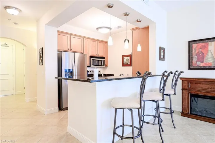 Kitchen featuring light tile patterned floors, dark stone countertops, hanging light fixtures, stainless steel appliances, and light brown cabinets