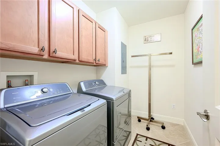 Laundry room featuring light tile patterned flooring, baseboards, independent washer and dryer, cabinet space, and electric panel