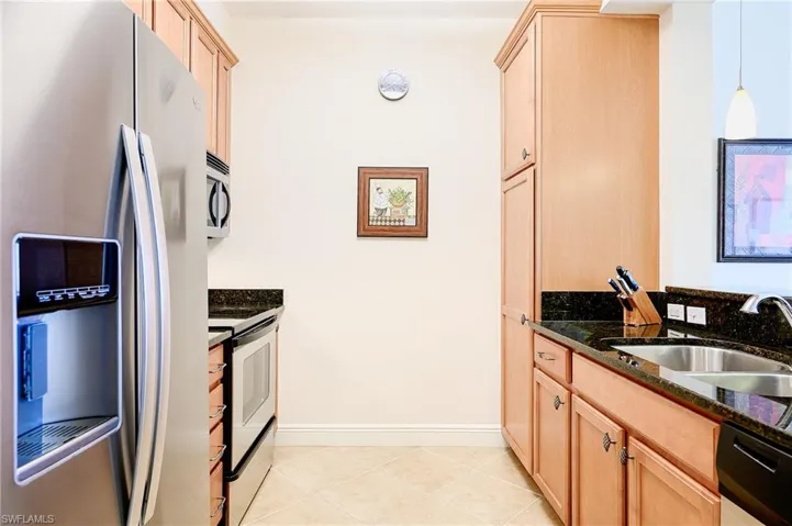 Kitchen featuring a sink, appliances with stainless steel finishes, light brown cabinetry, dark stone countertops, and decorative light fixtures