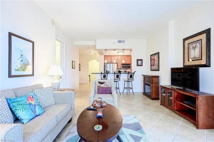 Living room with light tile patterned floors, visible vents, arched walkways, and baseboards