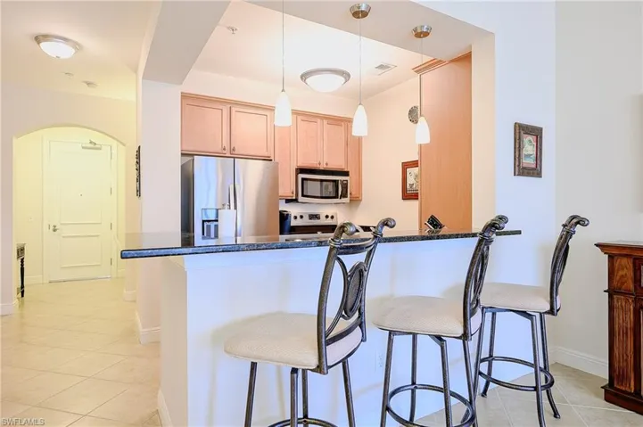 Kitchen featuring decorative light fixtures, a breakfast bar area, appliances with stainless steel finishes, dark stone countertops, and a peninsula