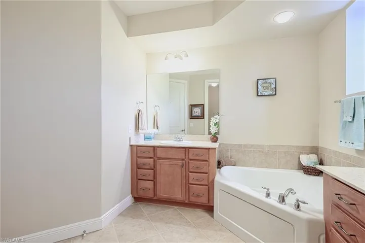 Bathroom featuring a garden tub, tile patterned flooring, vanity, and baseboards