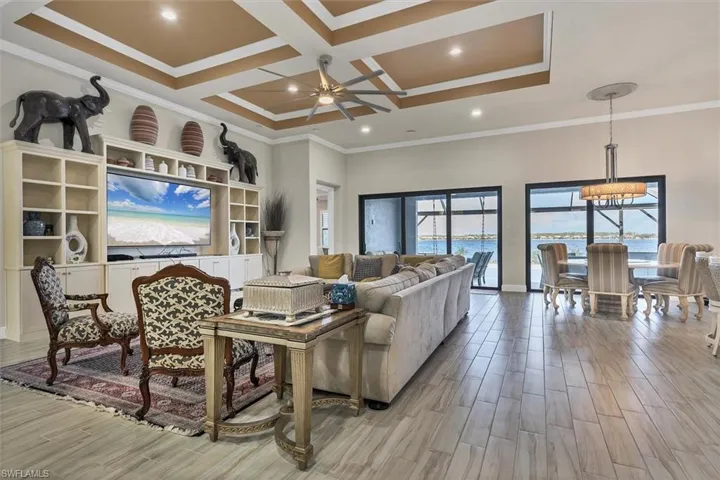 Living room featuring beam ceiling, coffered ceiling, crown molding, a water view, and ceiling fan with notable chandelier
