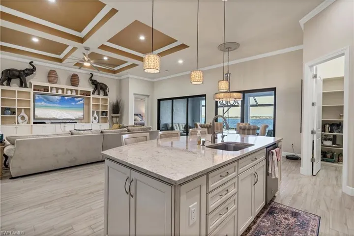 Kitchen with light stone counters, ceiling fan, a kitchen island with sink, crown molding, and sink