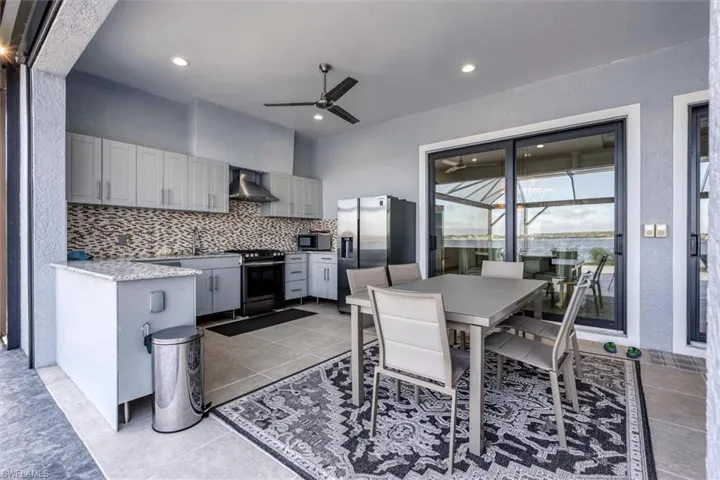 Kitchen featuring wall chimney range hood, ceiling fan, gray cabinets, tasteful backsplash, and stainless steel appliances