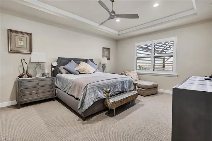 Bedroom featuring light colored carpet, a raised ceiling, and ceiling fan