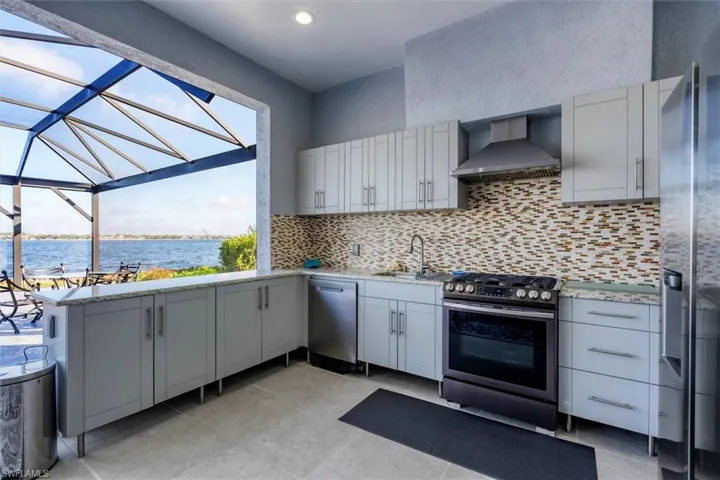 Kitchen featuring decorative backsplash, stainless steel appliances, sink, wall chimney range hood, and a water view