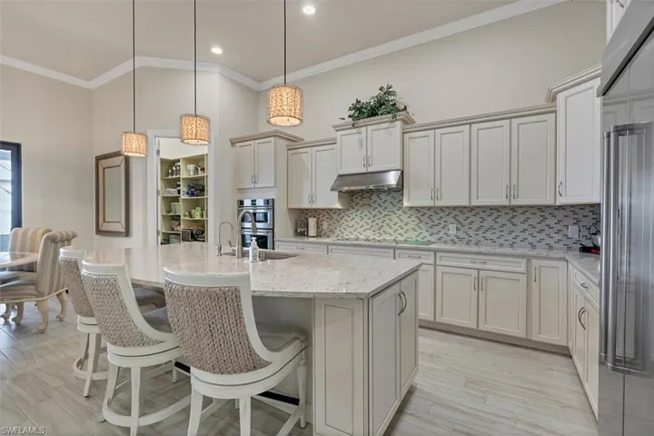 Kitchen featuring pendant lighting, an island with sink, appliances with stainless steel finishes, tasteful backsplash, and light stone counters