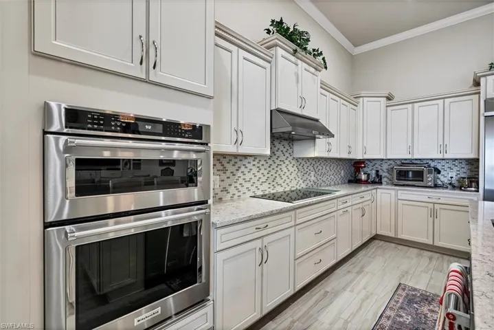 Kitchen with light stone countertops, tasteful backsplash, double oven, crown molding, and black electric cooktop