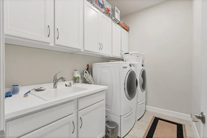 Clothes washing area with washer and clothes dryer, cabinets, and sink