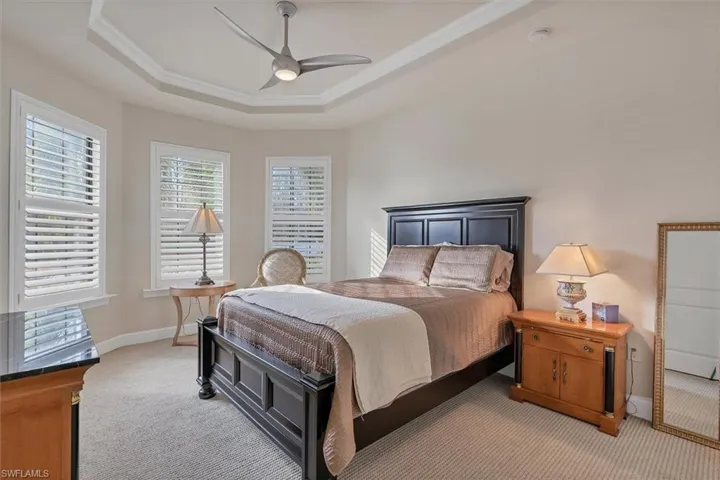 Carpeted bedroom with ceiling fan, a raised ceiling, and crown molding