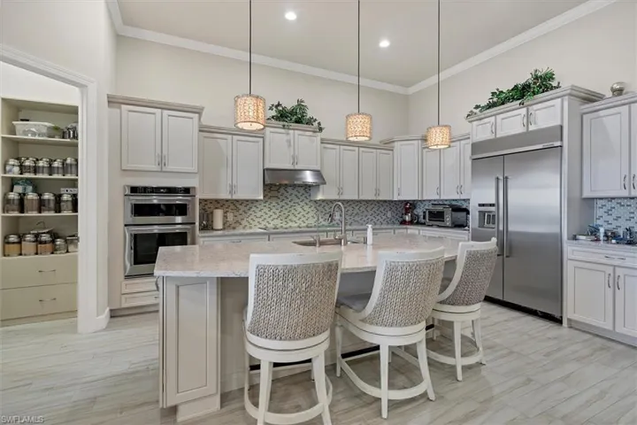Kitchen with light stone countertops, appliances with stainless steel finishes, decorative light fixtures, and an island with sink