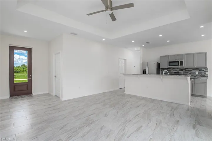 Front entrance, kitchen with gray cabinets, stainless steel appliances, a raised ceiling, recessed lighting, and a kitchen island with sink.