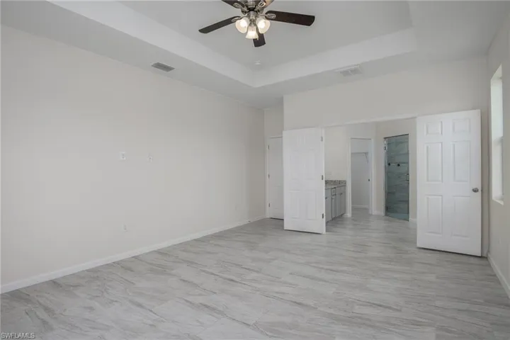 Master bedroom or bedroom #4 featuring a raised ceiling, double door entry to ensuite bath, and ceiling fan