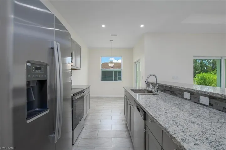 Kitchen featuring stainless steel appliances, light stone countertops, recessed lighting, hanging light fixtures, gray cabinets, and view of dining area