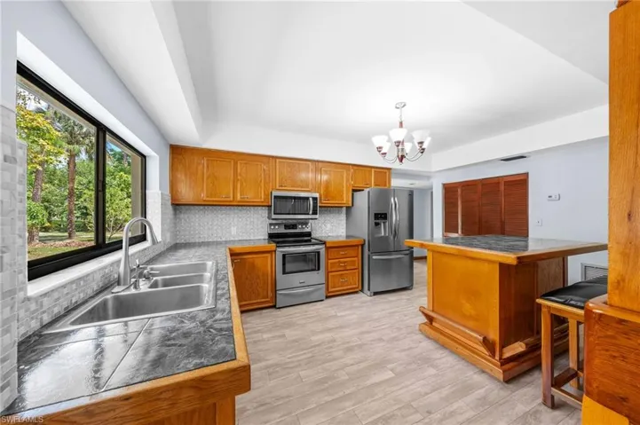 Kitchen featuring a notable chandelier, backsplash, brown cabinetry, appliances with stainless steel finishes, and a sink