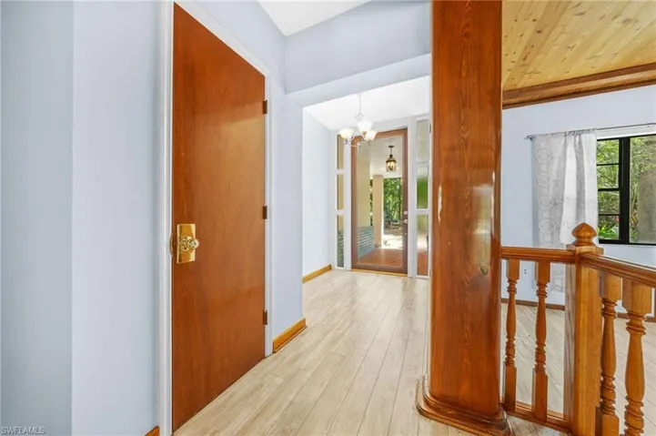 Hall with wood finished floors, a notable chandelier, and baseboards