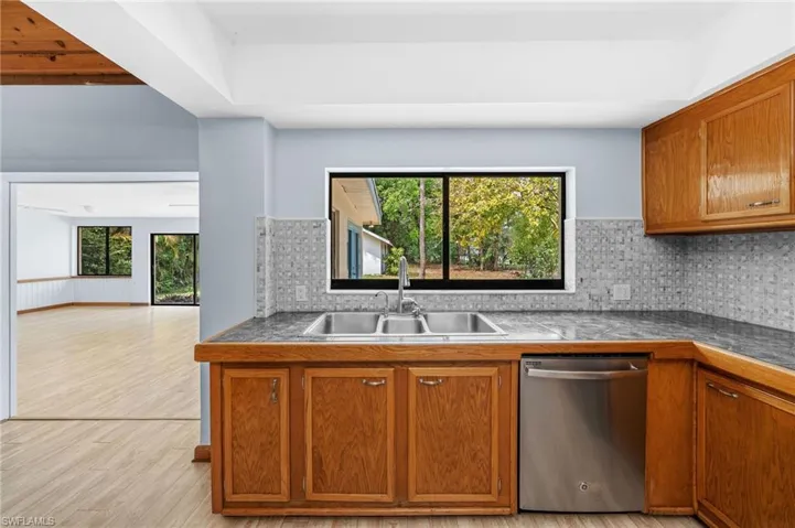 Kitchen featuring stainless steel dishwasher, tasteful backsplash, light wood-type flooring, a sink, and brown cabinets