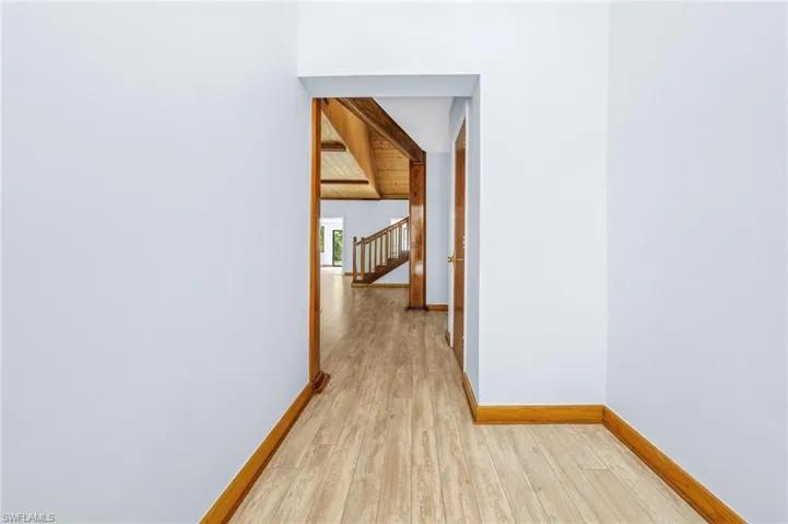 Hall with light wood-style flooring, baseboards, and vaulted ceiling with beams
