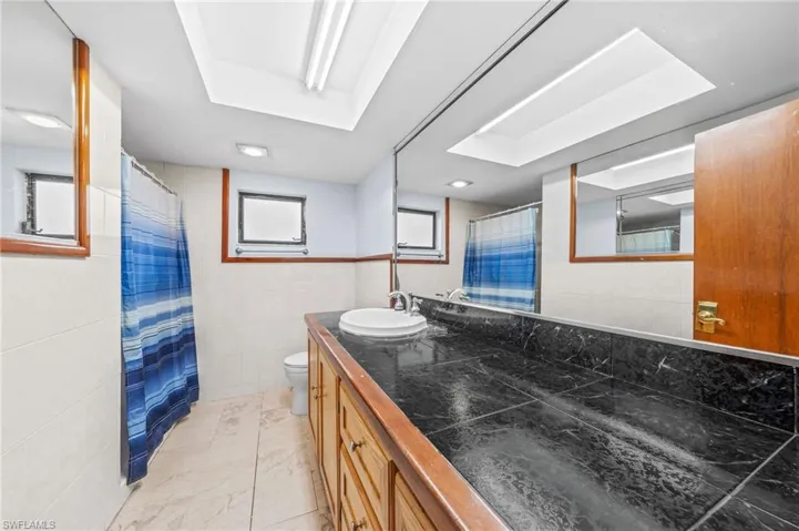 Full bath with a shower with curtain, vanity, toilet, marble finish floor, and tile walls