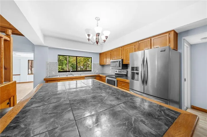 Kitchen with pendant lighting, appliances with stainless steel finishes, a notable chandelier, backsplash, and baseboards