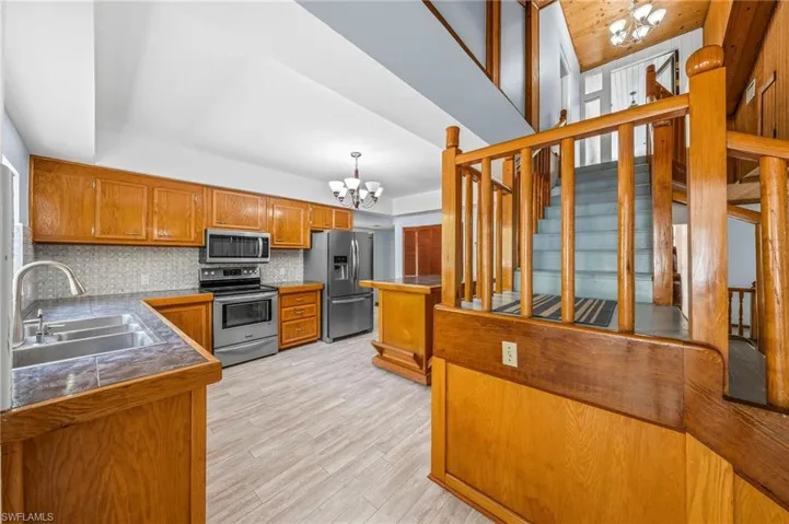 Kitchen with tasteful backsplash, a notable chandelier, brown cabinetry, appliances with stainless steel finishes, and a sink