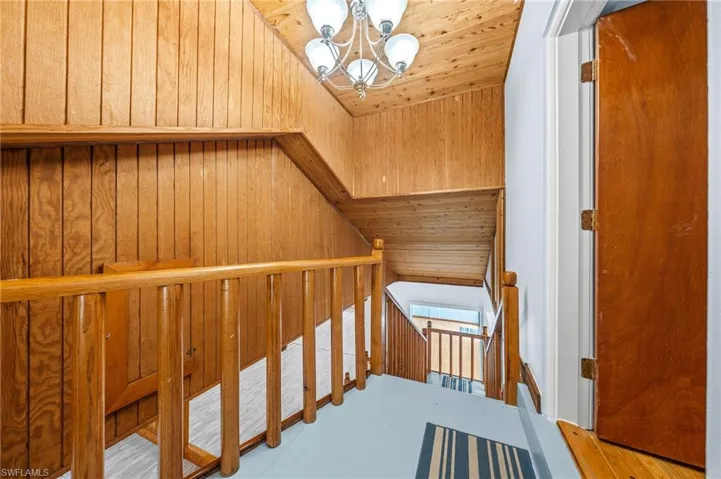 Staircase featuring wood walls, a notable chandelier, and wood ceiling