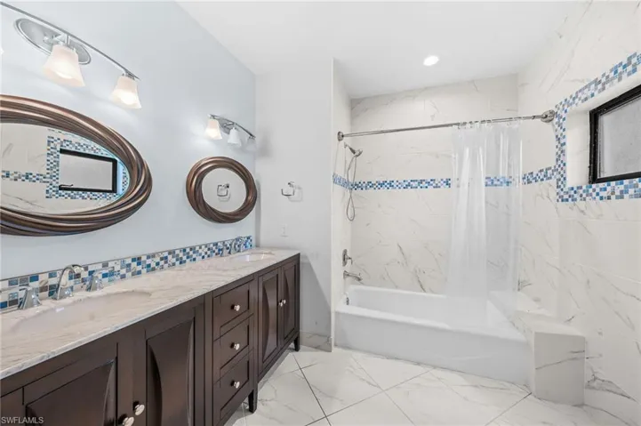 Bathroom with shower / bath combo, double vanity, marble finish floor, and a sink