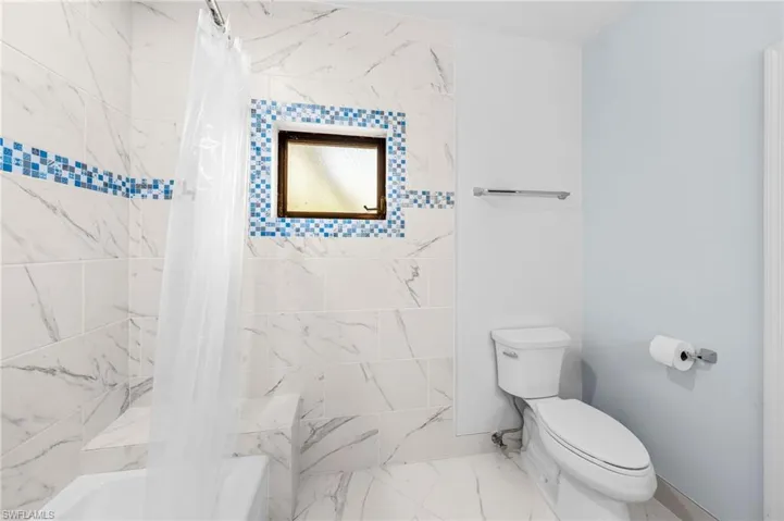 Full bathroom featuring shower / bath combo with shower curtain, marble finish floor, and toilet