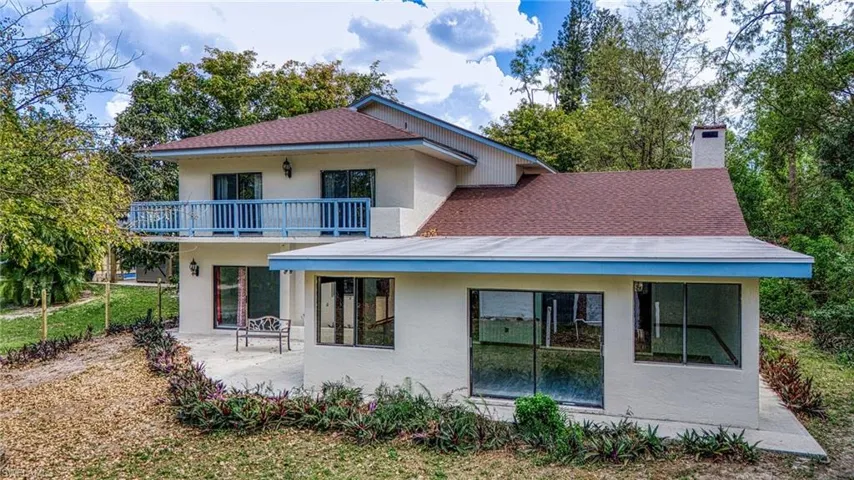 Rear view of house with a balcony, stucco siding, a chimney, a patio area, and a shingled roof