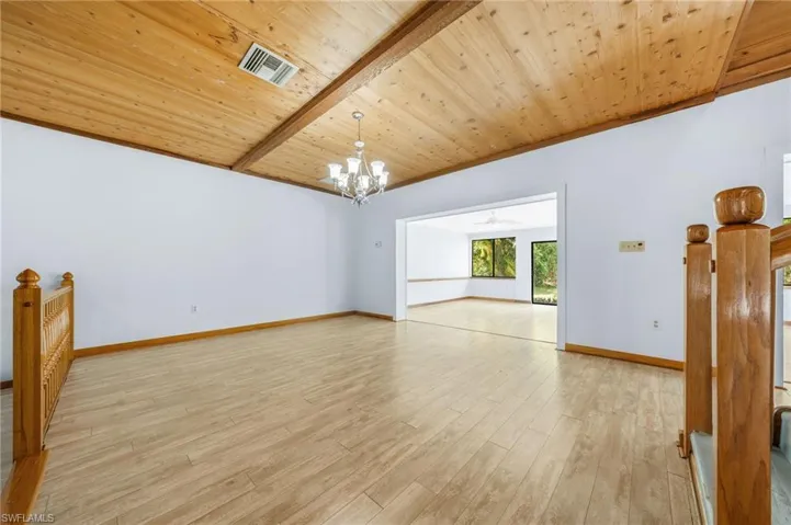 Spare room featuring light wood-style flooring, visible vents, wood ceiling, baseboards, and a notable chandelier