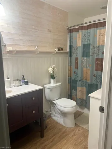 Full bathroom featuring vanity, wooden walls, curtained shower, light wood-style floors, and a wainscoted wall