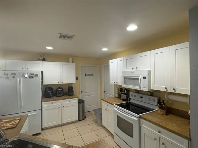 Kitchen featuring white appliances, white cabinetry, light tile patterned floors, recessed lighting, and dark countertops