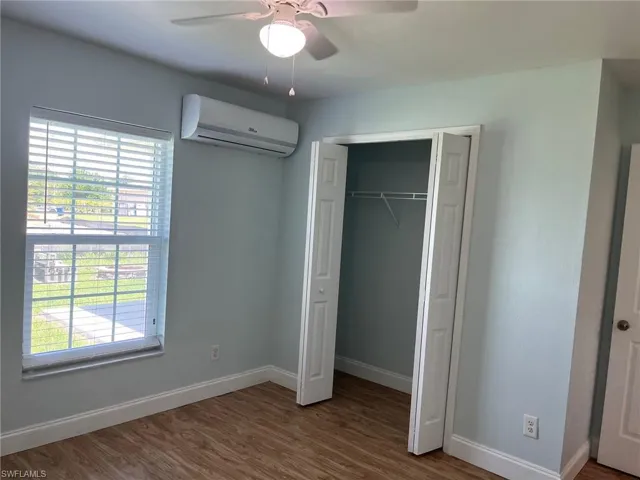Unfurnished bedroom with wood finished floors, a wall mounted air conditioner, a closet, and ceiling fan