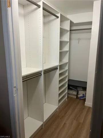 Walk in closet with dark wood-type flooring
