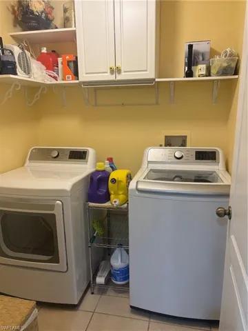 Washroom with cabinet space, light tile patterned floors, and washing machine and clothes dryer