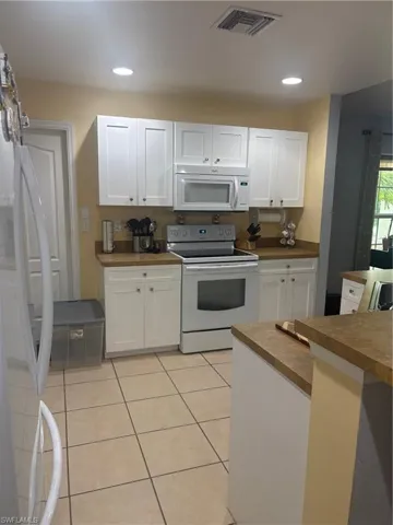 Kitchen with white cabinets, white appliances, light tile patterned floors, recessed lighting, and dark countertops
