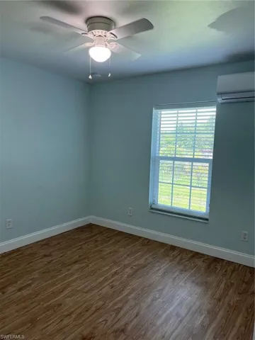 Empty room featuring dark wood-type flooring, a wall mounted AC, and ceiling fan