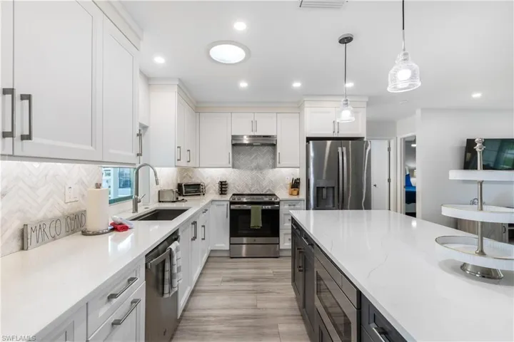 Kitchen featuring stainless steel appliances, white cabinets, light stone counters, decorative light fixtures, and recessed lighting