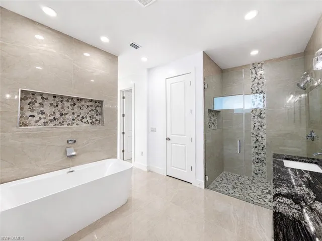Modern bathroom featuring a freestanding tub, glass-enclosed shower, and a vanity with a dark stone countertop