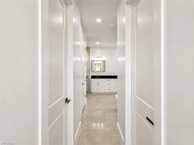 Hallway featuring white paneled doors with dark hardware, recessed lighting, and polished tile flooring